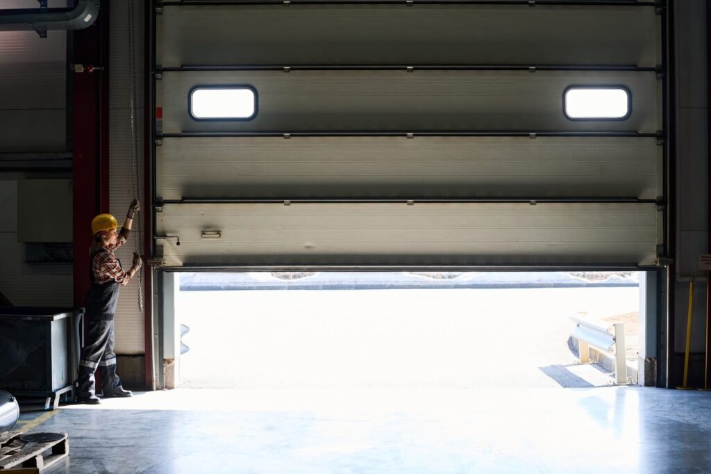 Young female worker of factory or hangar opening shutter roller door